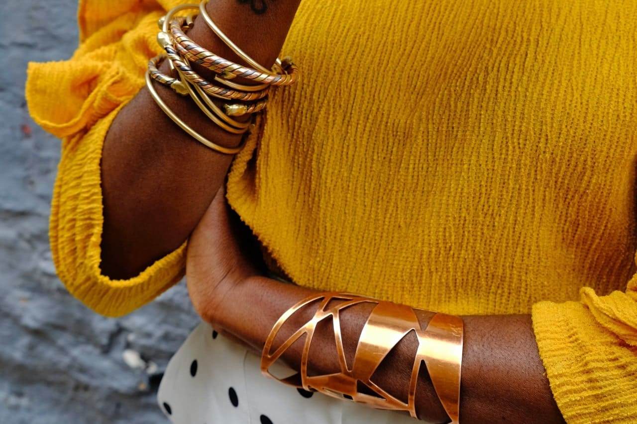 close up image of a woman's arms adorned with yellow gold cuff bracelets