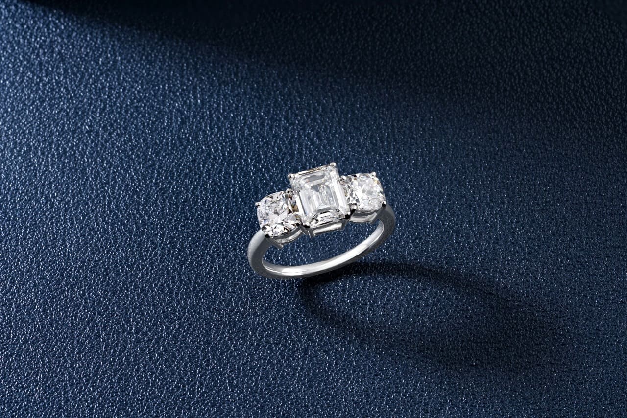 A three stone, silver engagement ring featuring an emerald cut diamond and two princess cut accent stones