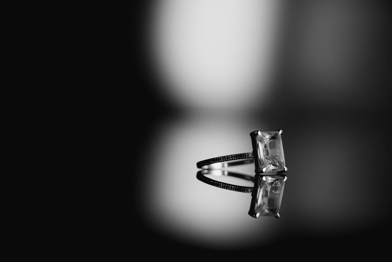 Black and white image an emerald cut engagement ring sitting on a mirrored surface