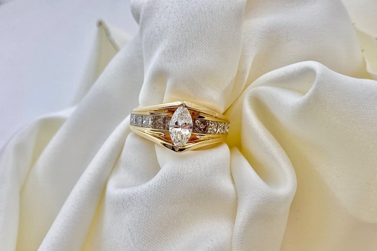 A unique gold engagement ring with a marquise diamond center stone on a piece of white fabric