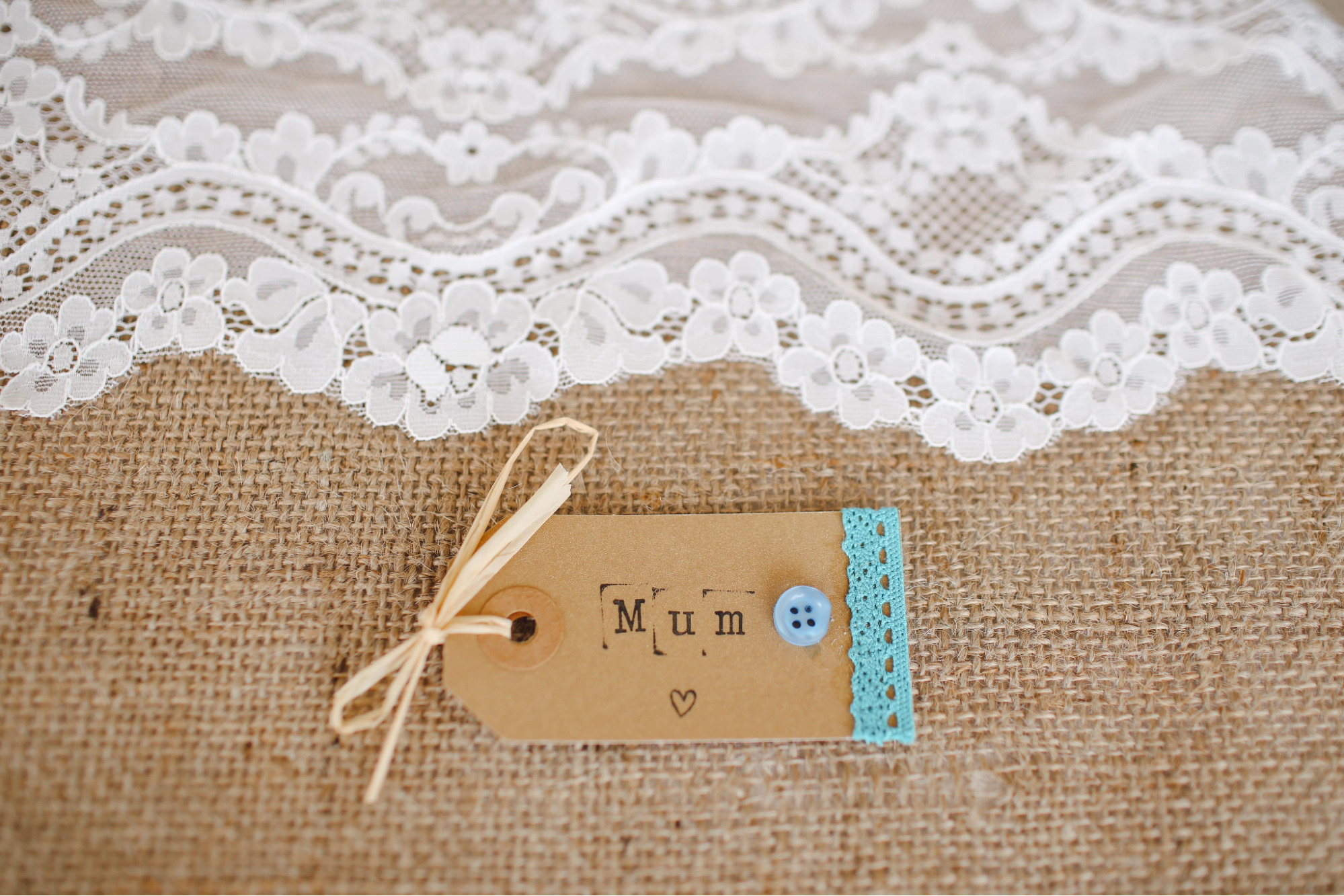 A handmade gift tag for a Mother’s Day present is on a burlap and lace table runner