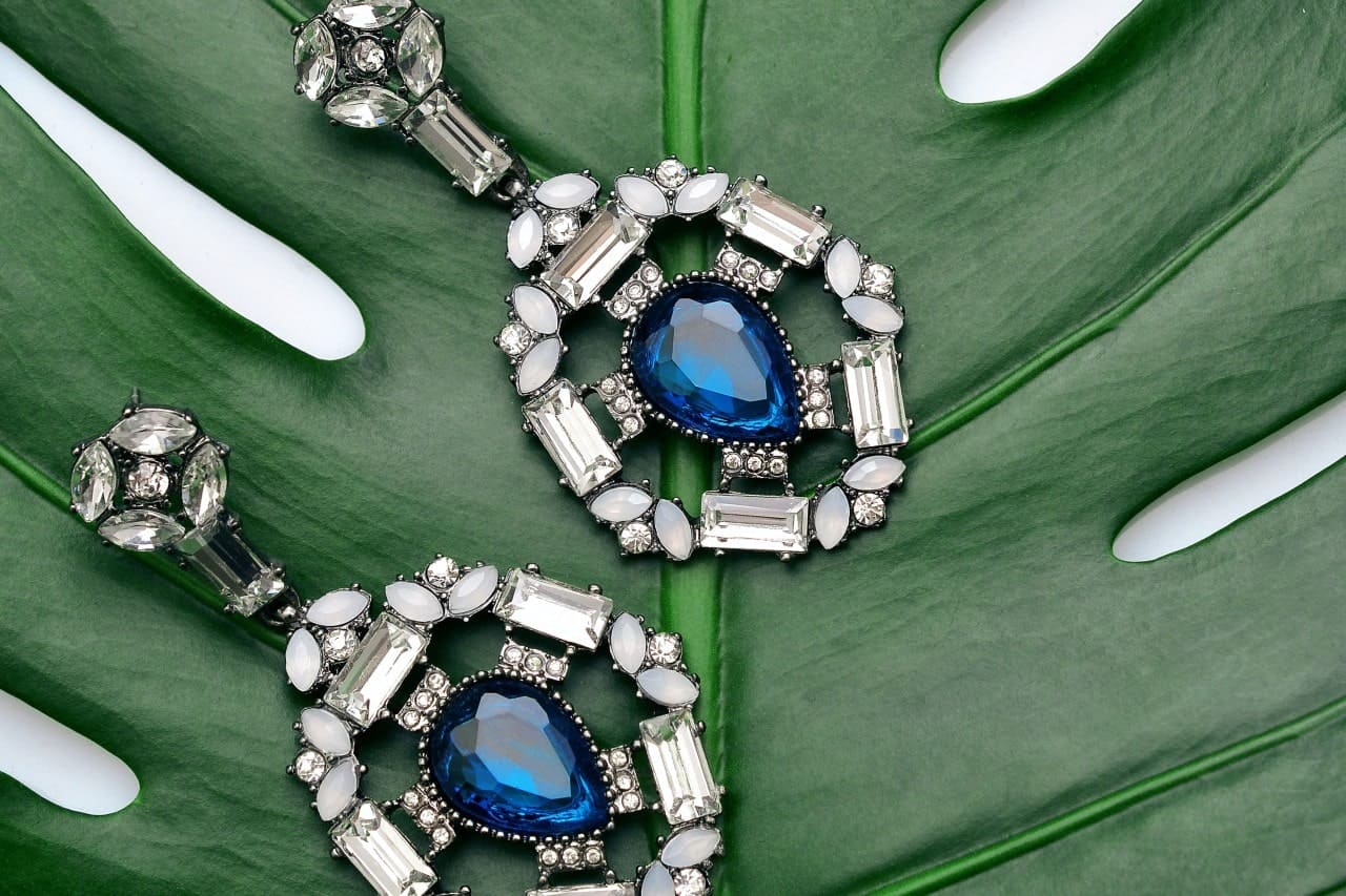 Pair of gemstone and diamond earrings on a palm frond.
