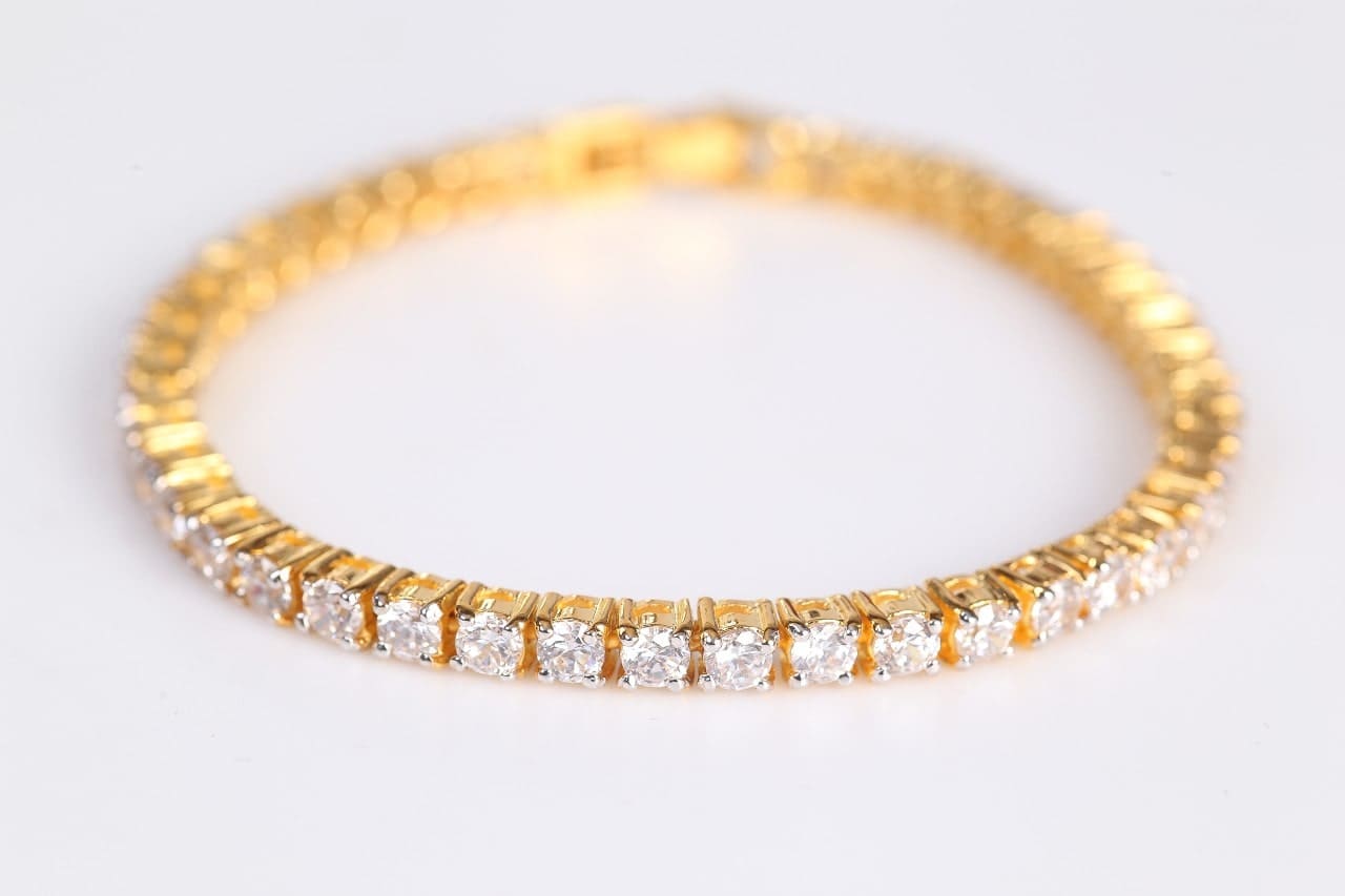 a yellow gold diamond tennis bracelets lying on a white surface