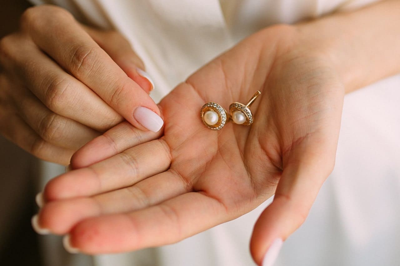 a bride holding a pair of pear stud earrings in her hand.