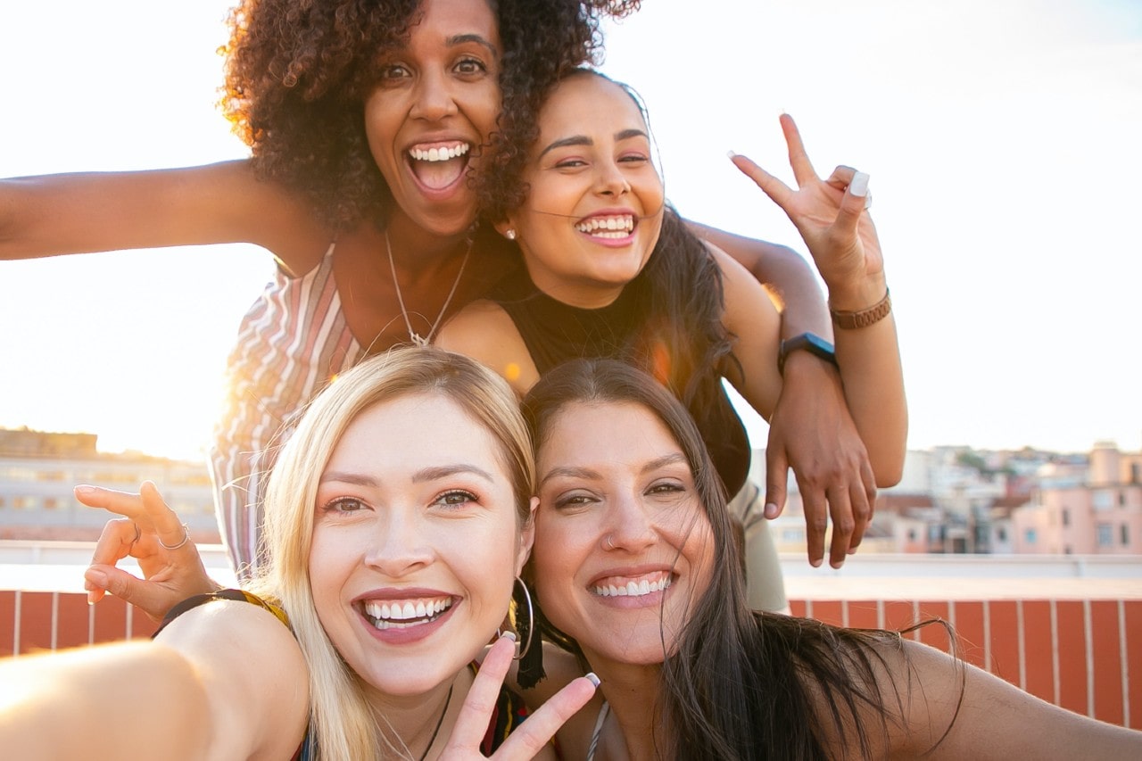 a group of friends wearing fine jewelry take a selfie on a rooftop.