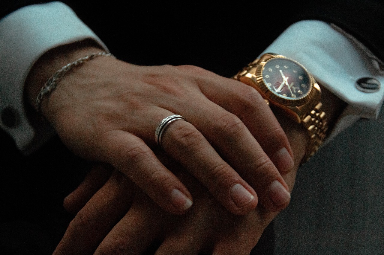 close up image of a person’s hands, their yellow gold watch, and white gold wedding band