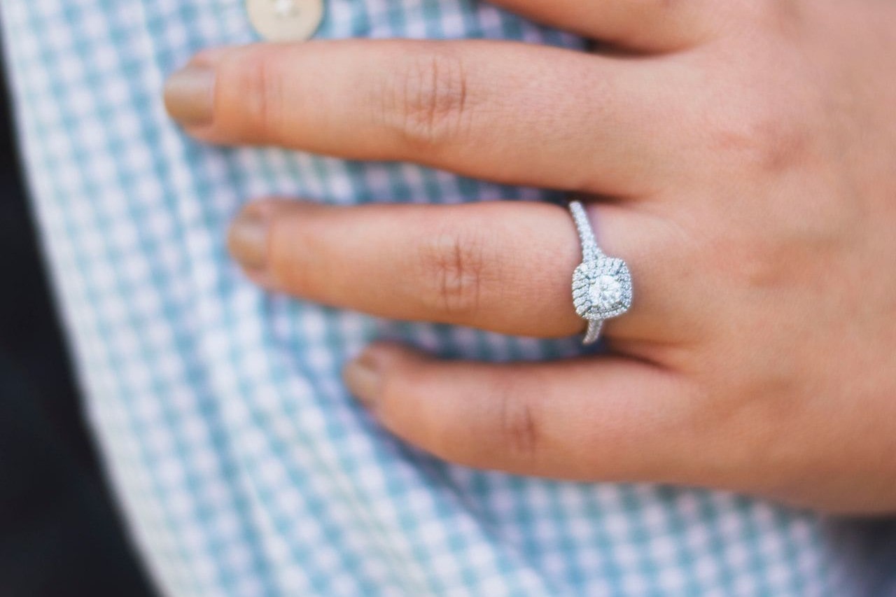 A woman with a round-cut halo engagement ring from A.JAFFE touches her fiance’s arm