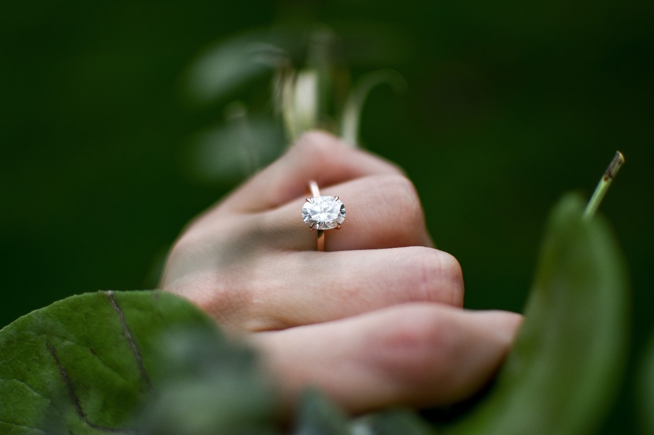 a woman holding a plant wears a gold solitaire engagement ring.