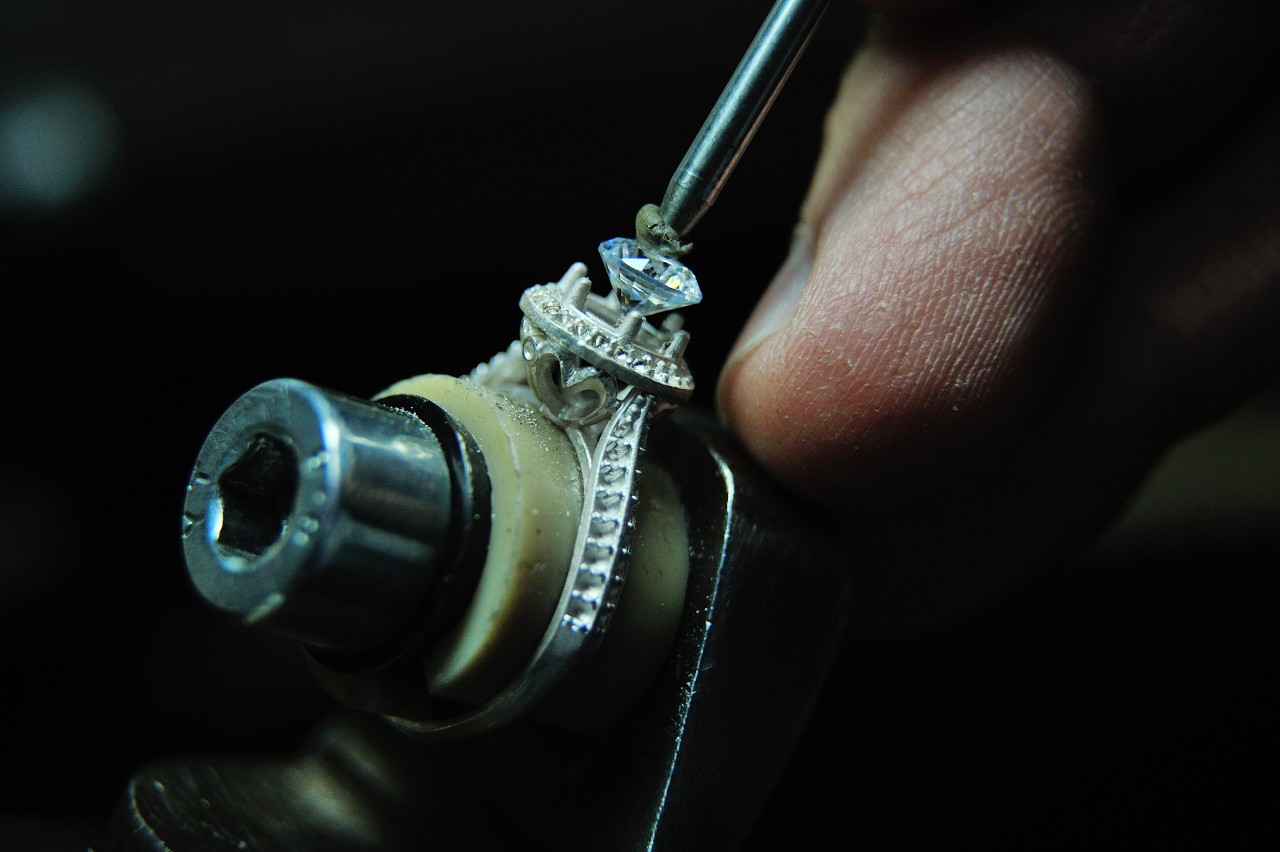 A jeweler sets a natural, round-cut diamond into a halo engagement ring design.