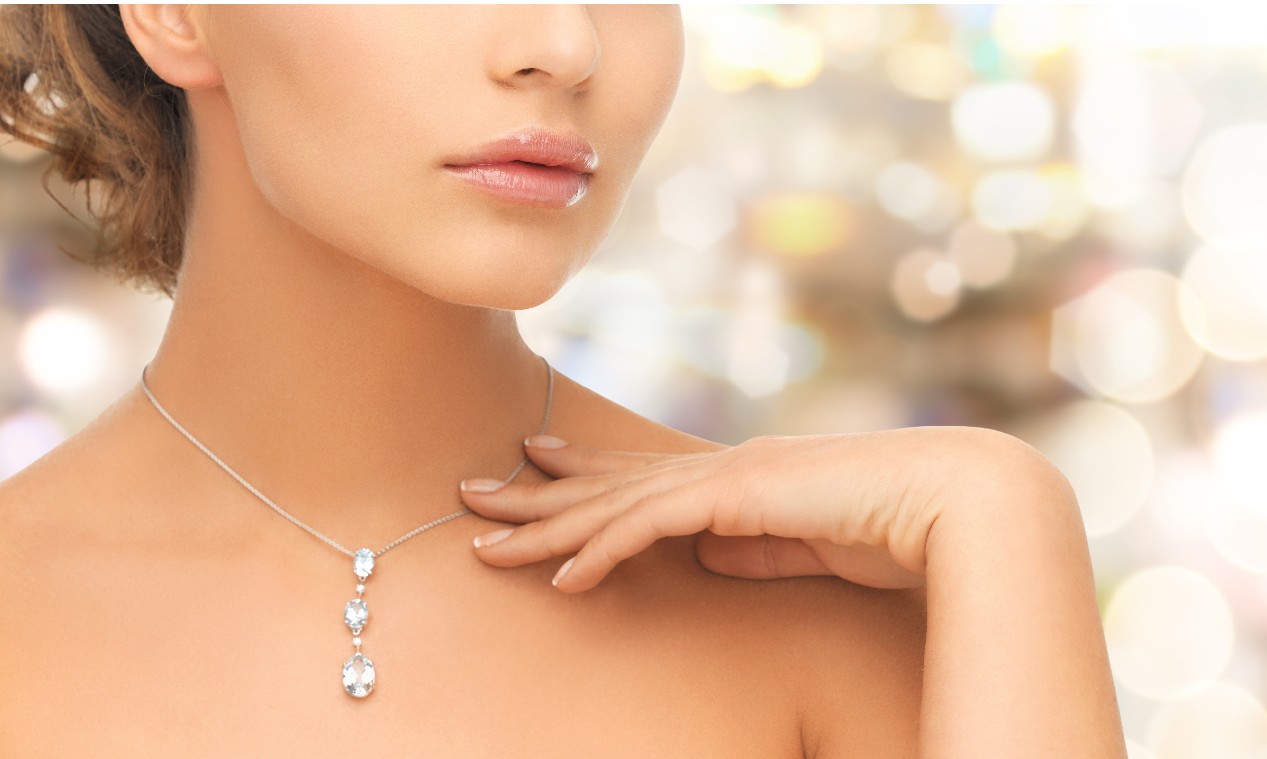 A woman standing in front of fairy lights touches her white gold diamond necklace.