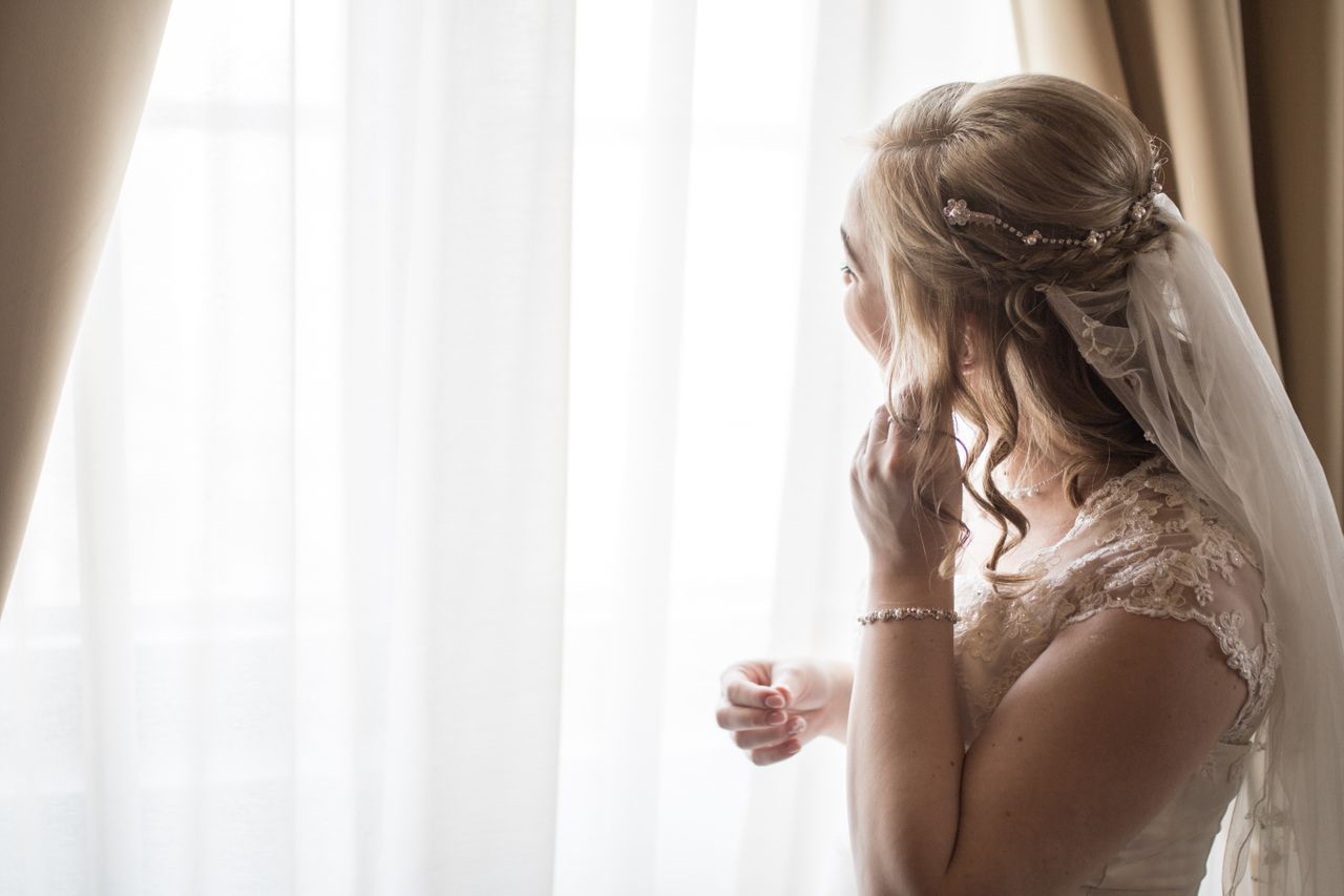 A bride looks out the window as she puts on her earrings.